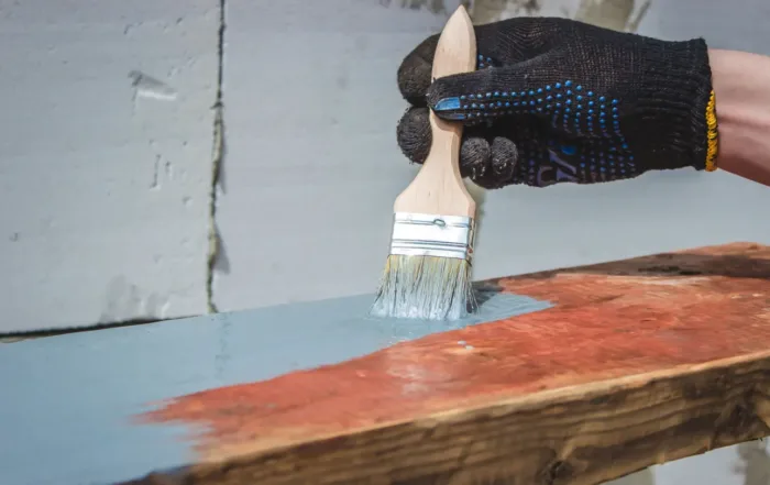 A hand holding a brush that is painting a piece of timer gray